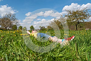 Child boy lies in grass in dandelions field and rejoices in sun. Summer vacation in the countryside