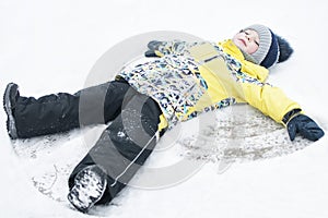 A child, a boy, lies on the snow, makes a snow angel with his arms and legs, emotions, laughs