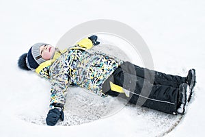 A child, a boy, lies on the snow, makes a snow angel with his arms and legs, emotions, laughs