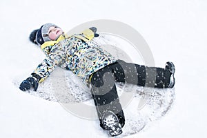 A child, a boy, lies on the snow, makes a snow angel with his arms and legs, emotions, laughs