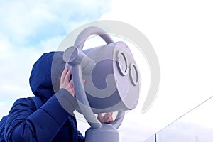 Child boy looks through binoculars in winter on overcast sky background.