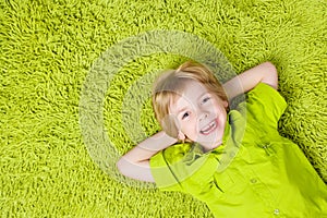 Child Boy lying on green carpet background. Smiling Kid