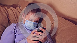 Child boy in a mask using a smartphone browses social networks.