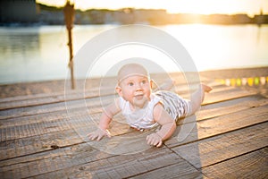 A child a boy, one year old, blond man lies on his stomach on wooden dock, pier in striped clothes, compound near pond on sandy be