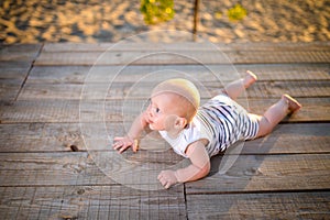 A child a boy, one year old, blond man lies on his stomach on wooden dock, pier in striped clothes, compound near pond on sandy be