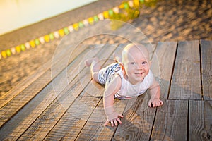 A child a boy, one year old, blond man lies on his stomach on wooden dock, pier in striped clothes, compound near pond on sandy be