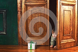 Child boy peeks out of the door with a christmas gift box