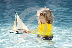 Child boy play on the beach on a sunny day. Little sailor play with sailing boat in sea water. Child dreams of travel