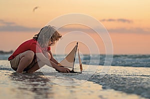 Child boy play on the beach on a sunny day. Little sailor play with sailing boat in sea water. Child dreams of travel