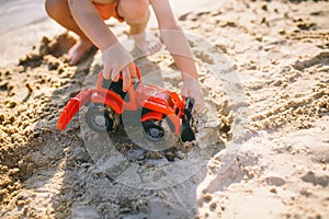 Child boy playing on the beach near the river toy red tractor