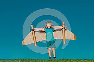 Child boy playing with cardboard toy airplane wings craft in sky. Kid dreaming of flying. Kid dreams of future. Blonde