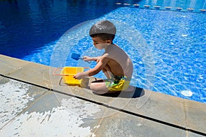 Child boy playing with his toys on the edge of a swimming pool