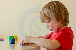 child boy playing with plasticine while sitting at table, side view. childhood, developing activities for children