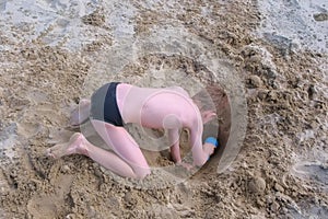 Child boy playing on sand beach digging shovel deep hole on summer vacation.