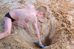 Child boy playing on sea sand beach digging shovel deep hole and throwing sand.