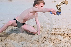 Child boy playing on sea sand beach digging shovel deep hole and throwing sand.