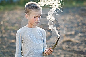 Child boy playing with smoking wooden stick outdoors