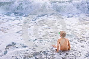 Child boy playing in the waves on the beach in summer sunset, kid watching sea waves and having fun