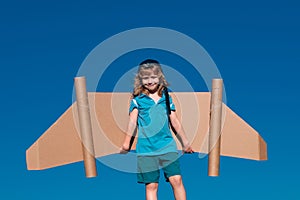 Child boy plays in an astronaut dreams of space. Happy child play with toy plane cardboard wings against blue sky. Kid