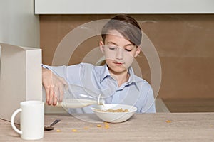 Child boy pours cornflakes into a white plate. The child prepares a breakfast.