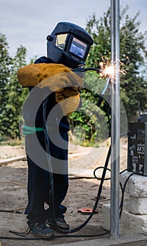 A child, a boy pretends to weld a fence. Welder`s costume, gloves, mask.