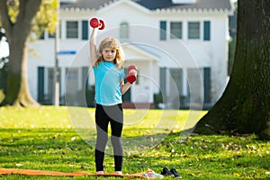 Child boy raising a dumbbell. Cute child training with dumbbells. Children fitness. Kid boy exercising with dumbbells