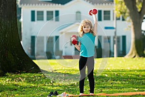 Child boy raising a dumbbell. Cute child training with dumbbells. Children fitness. Kid boy exercising with dumbbells