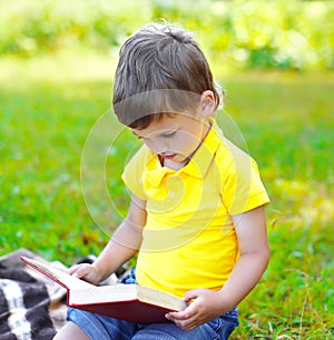 Child boy reading a book on the grass in summer