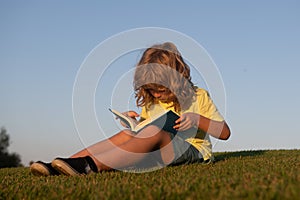 Child boy is reading a book on the spring park. Relaxing on the grass in the garden. Outdoor education. Kids success