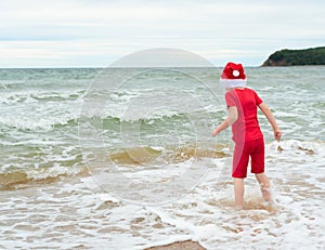 Child boy in red cloth and Santa Claus hat enjoying Christmas on the beach on Xmas travel vacation. Christmas or New