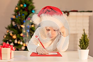 Child boy in red Santa hat writing a letter to Santa Claus. Christmas or New Year cozy holidays concept. Xmas time