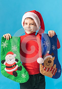 Child boy in red sweater and Santa hat with Christmas socks on blue background. Xmas and holidays concept. Generation