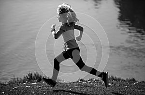 Child boy running or jogging near lake on grass in park. Little runners jogging outdoors in summer nature. Sporty child