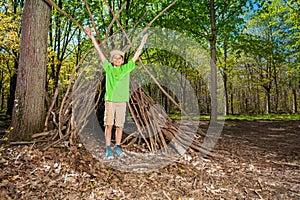 Child with boy-scout hat plain in the forest hut of branches