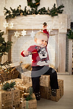 Child boy is sitting on the gift boxes against the background of the Christmas tree.