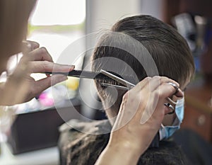 Child boy sitting in a mask at the hairdresser cutting a haircut