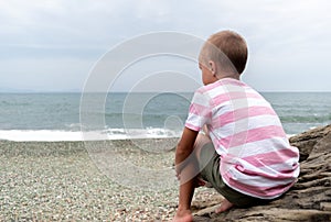 Child boy sitting on rocks by the ocean. Adventure by the sea