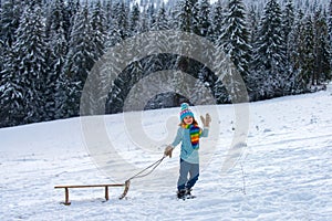 Child boy sledding in winter. Kid riding on snow slides in winter.