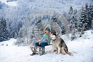 Child boy sledding in winter. Kid riding on snow slides in winter with dog husky.