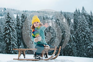 Child boy sledding in winter, playing with snowball. Kid riding on snow slides in winter. Winter christmas forest with
