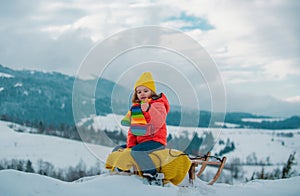 Child boy sledding in winter. Winter fun kids activities. Kid riding on snow slides in winter.