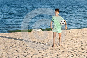 Child boy soccer player holding ball and ready for game or match on sandy beach. Beach football, sport, summer holidays