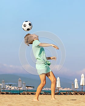 Child boy soccer player plays with soccer ball while having fun on sea beach. Kids games and leisure, summer holidays
