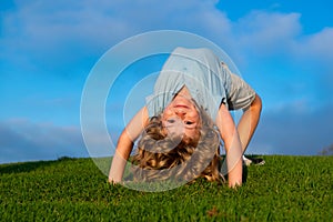 Child boy standing upside down on green grass in summer Park. The concept of a healthy family lifestyle. The fun and
