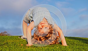 Child boy standing upside down on green grass in summer Park. The concept of a healthy family lifestyle. The fun and