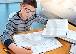 Child boy, student and writing on math book in studying, learning or education on table at home. Smart little kid busy