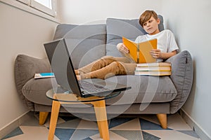 Child boy studying online at home with books and laptop