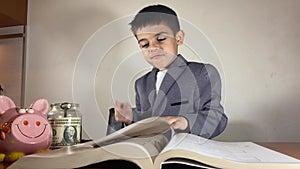 Child, boy in the suit thinking over the book turning the page and finds money. Investing in education concept