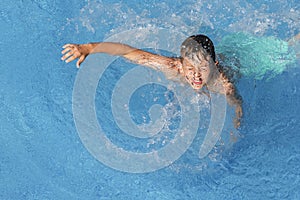 Child boy swim in blue water of hotel swimming pool at summer resort. Kids fun leisure activity. Water sports, vacation