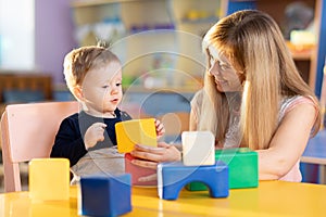 Child boy together with mother playing educational toys at sunny day in nursery